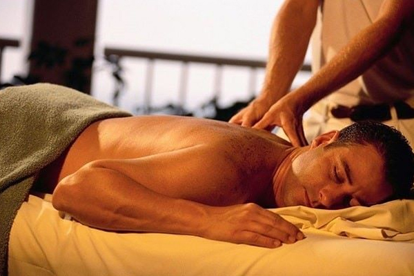 Người đàn ông nằm sấp trên bàn massage được mát-xa lưng trong phòng thư giãn.