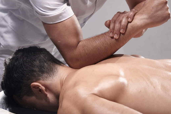 Kỹ thuật viên đang thực hiện vật lý trị liệu trên lưng trần người nam nằm sấp.