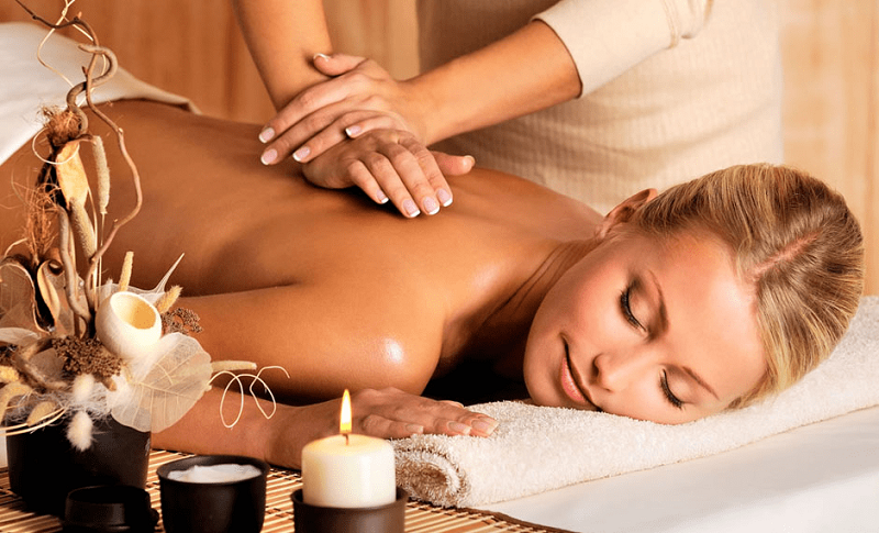 Phụ nữ đang nằm thư giãn khi được mát-xa lưng tại spa với nến và trang trí xung quanh.